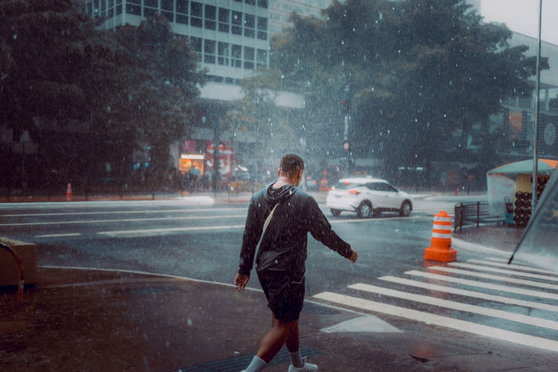 Man with a backpack crossing a city street in the rain