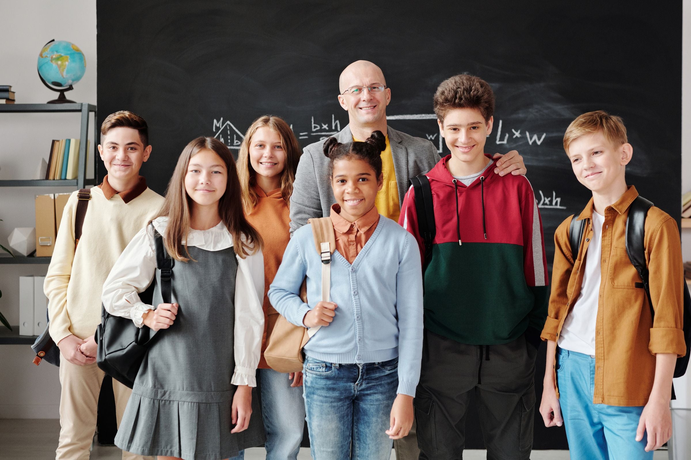 Teenage school students with backpacks smiling with their teacher